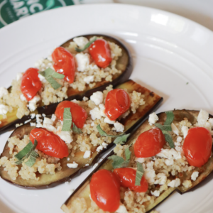A platter of grilled egplant slices topped with Ancient Harvest Traditional Quinoa, cherry tomatoes, feta cheese, and chopped herbs.